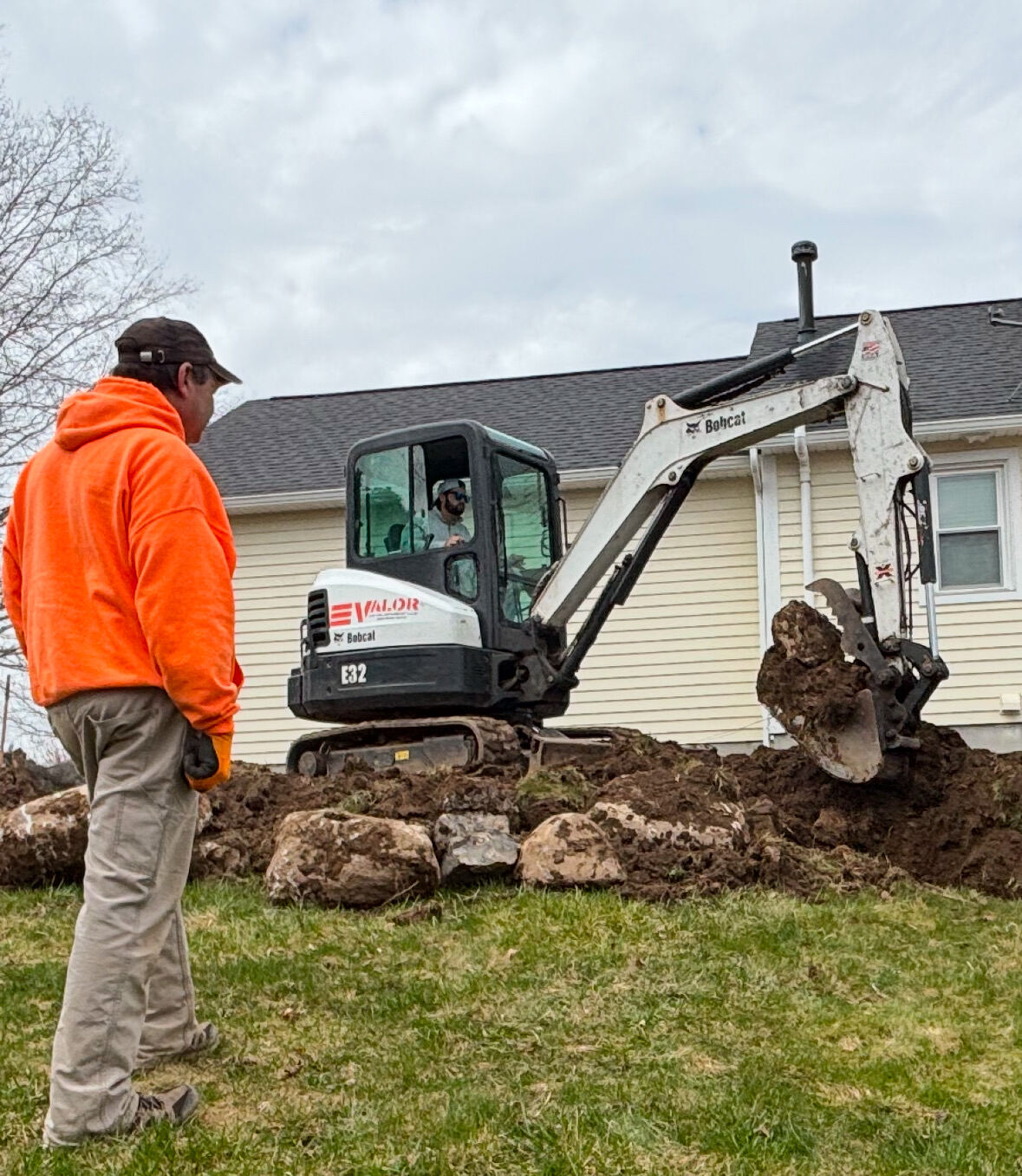 A VALOR crew member watching a mini excavator work beside a house